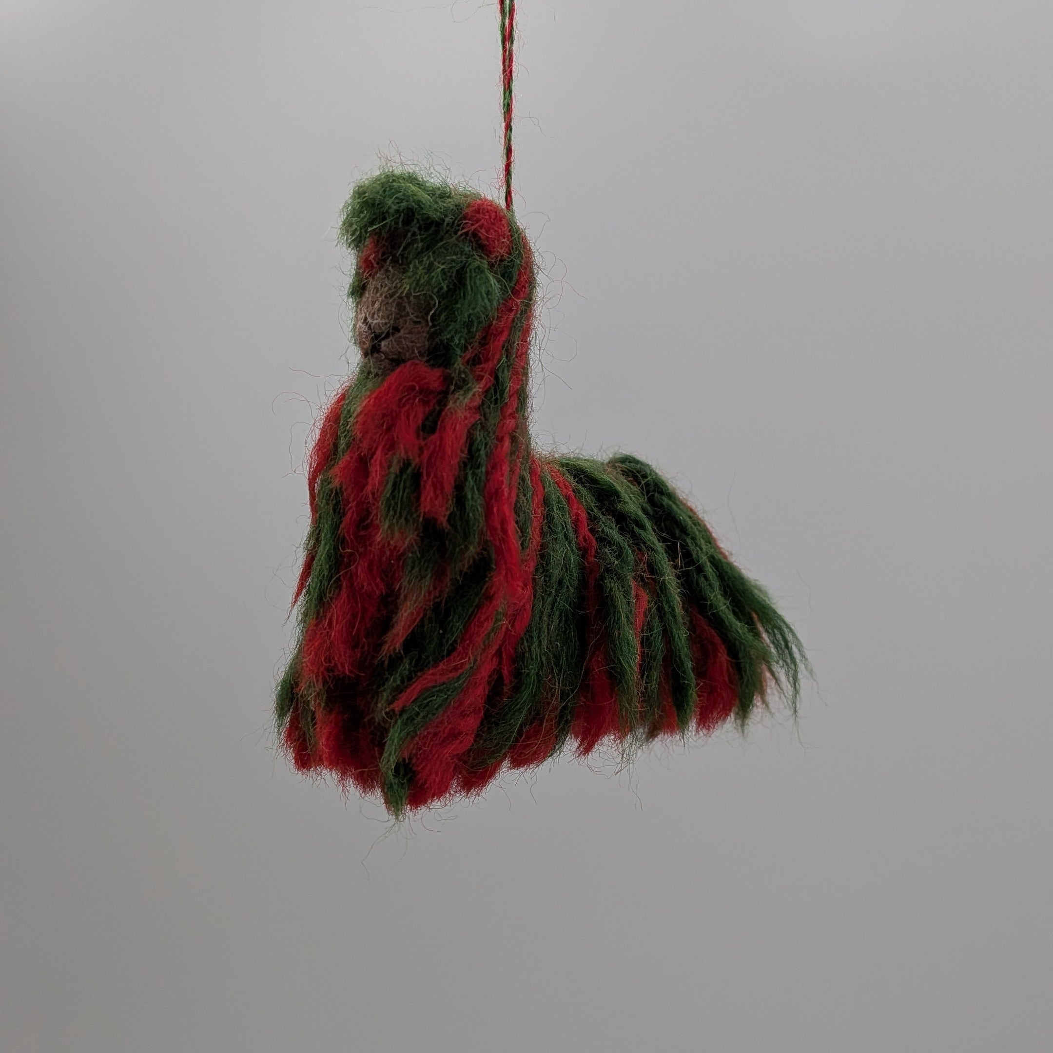 Decorative item resembling a horse made of red and green fabric hanging from a string against a white background.