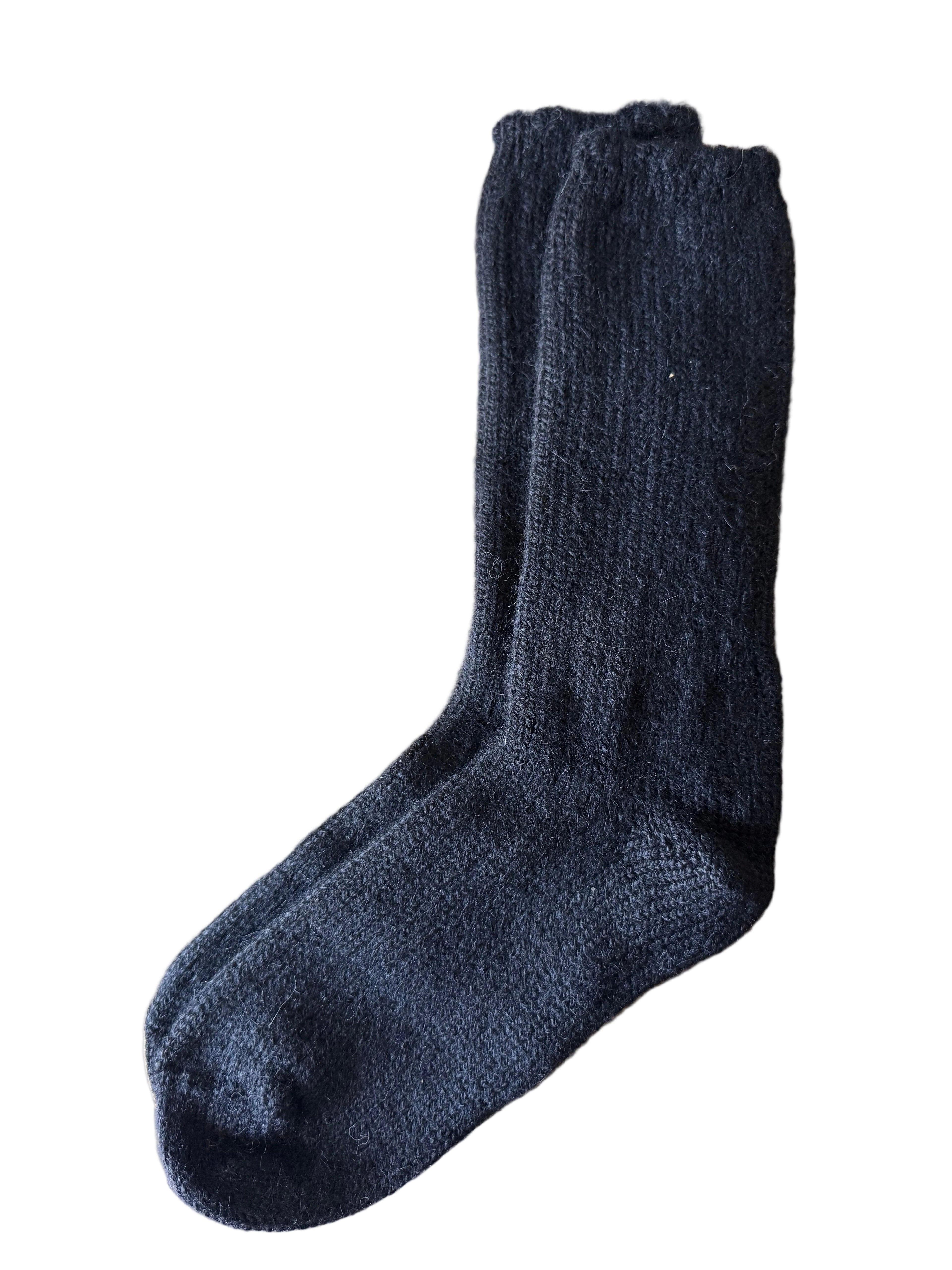 A single dark charcoal gray knit sock laid flat on a brown cardboard box, with a gray stone tile floor visible in the background.