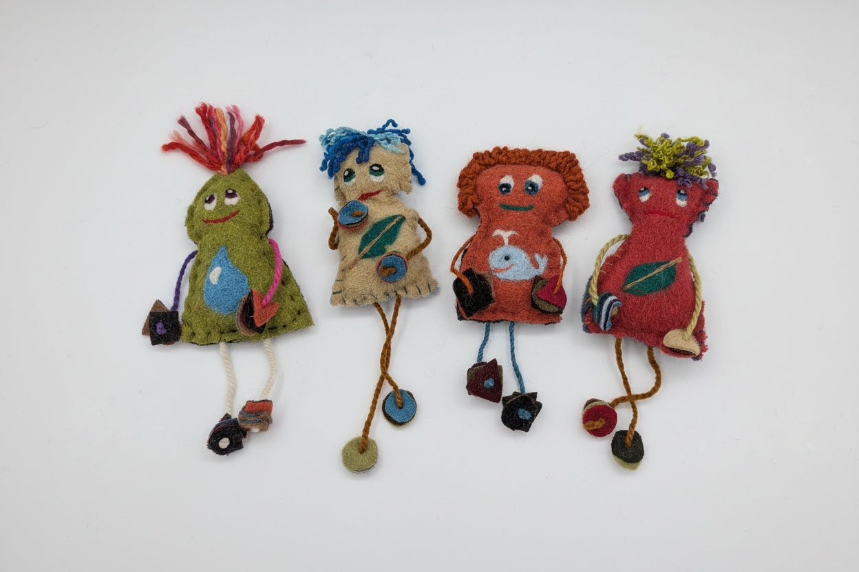 A group of handmade felt fabric creatures or dolls arranged on a plain white background. The figures are made from various colored felt materials with embroidered faces, yarn hair, and small dangling accessories.