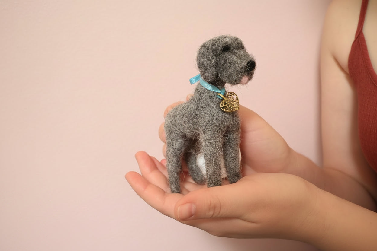 Small needle-felted dog held in hands with a textured gray background