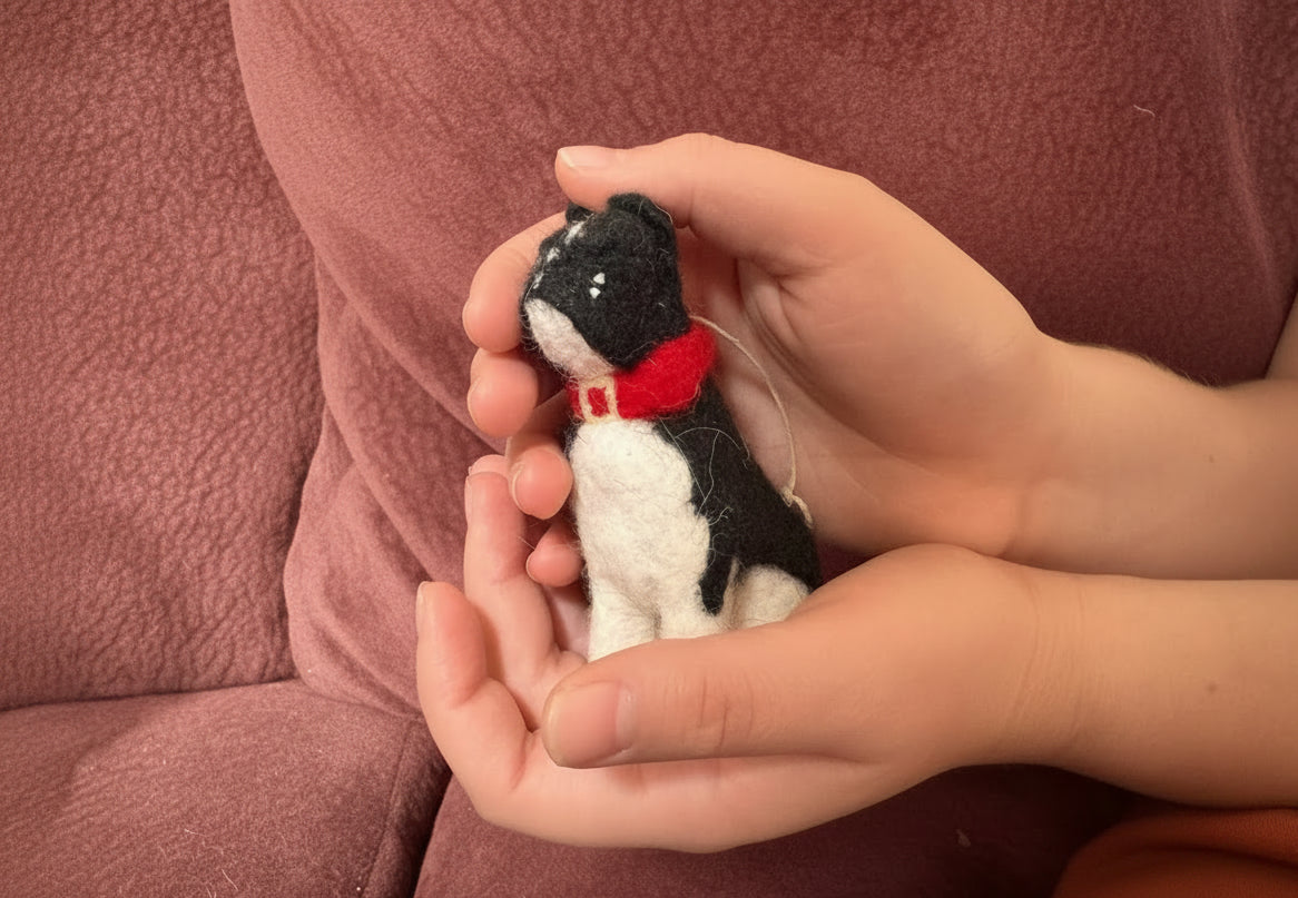 Hand holding a small felted french bulldog cradled in hands with a red collar