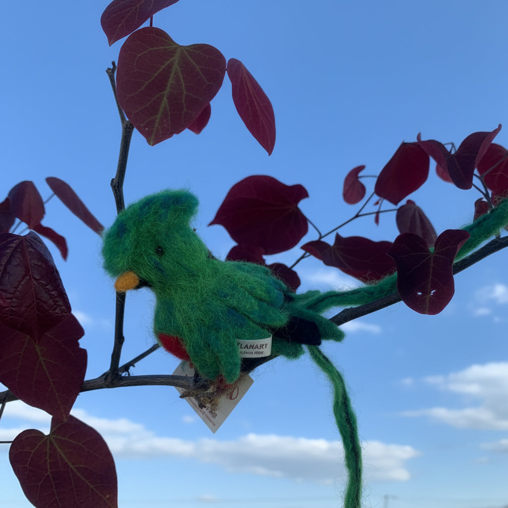 Green plush alpaca fiber Quetzal Bird ornament on a branch with red leaves