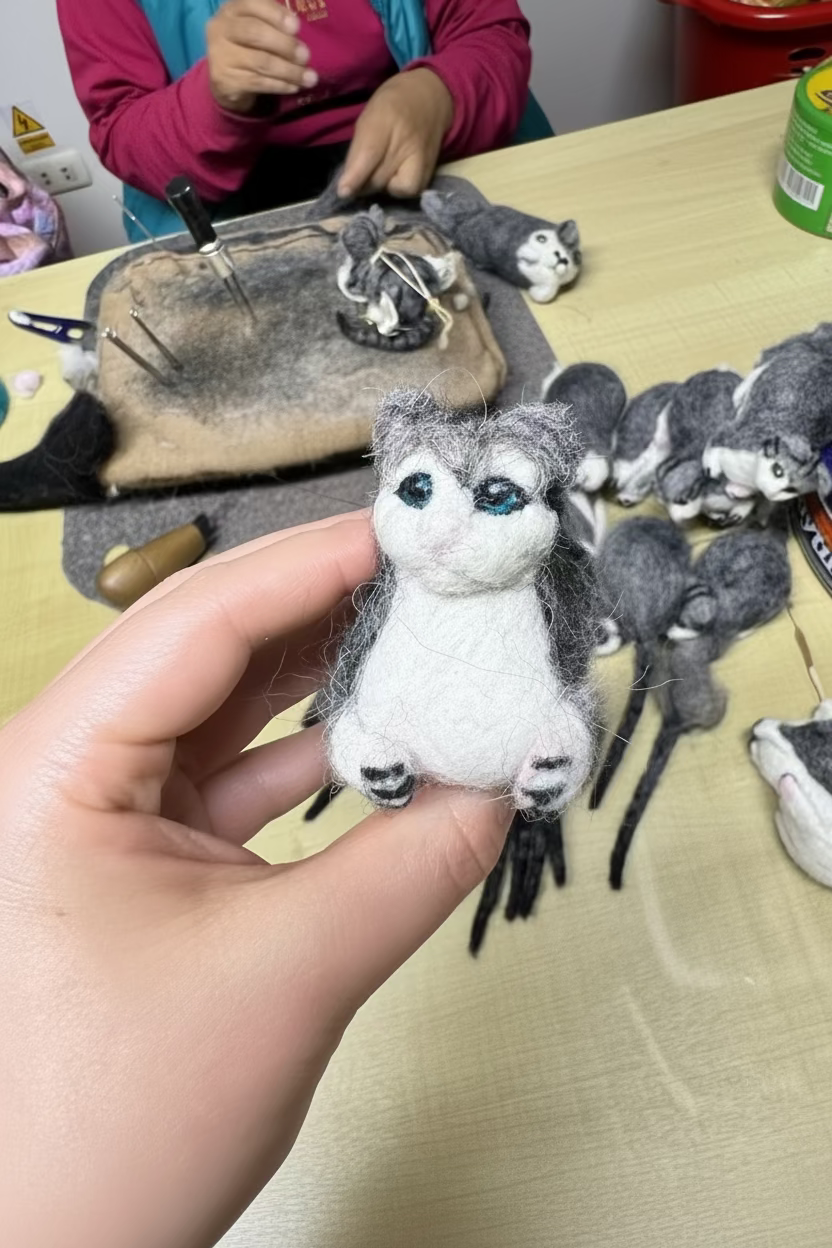 Hand holding a small felted animal toy with more toys on a table in the background.