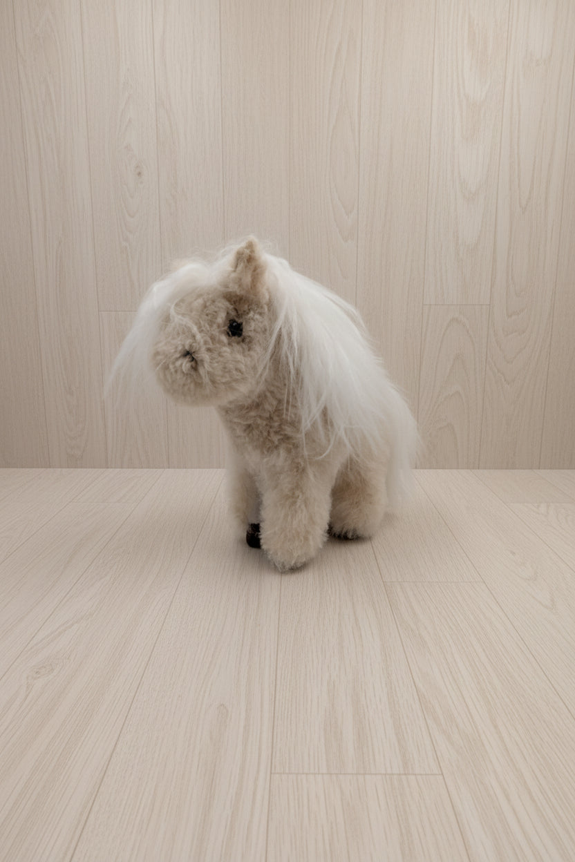 A small plush toy horse or pony with fluffy cream and white fur, standing on a plain white surface against a white background.