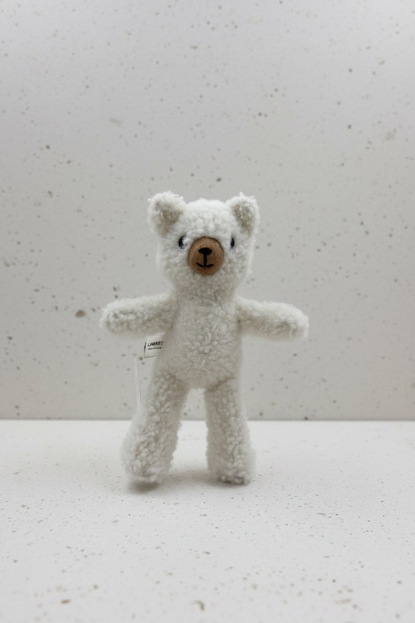 A small white teddy bear plush toy with a brown button nose and black embroidered eyes, mounted on a clear stand against a plain light gray wall.