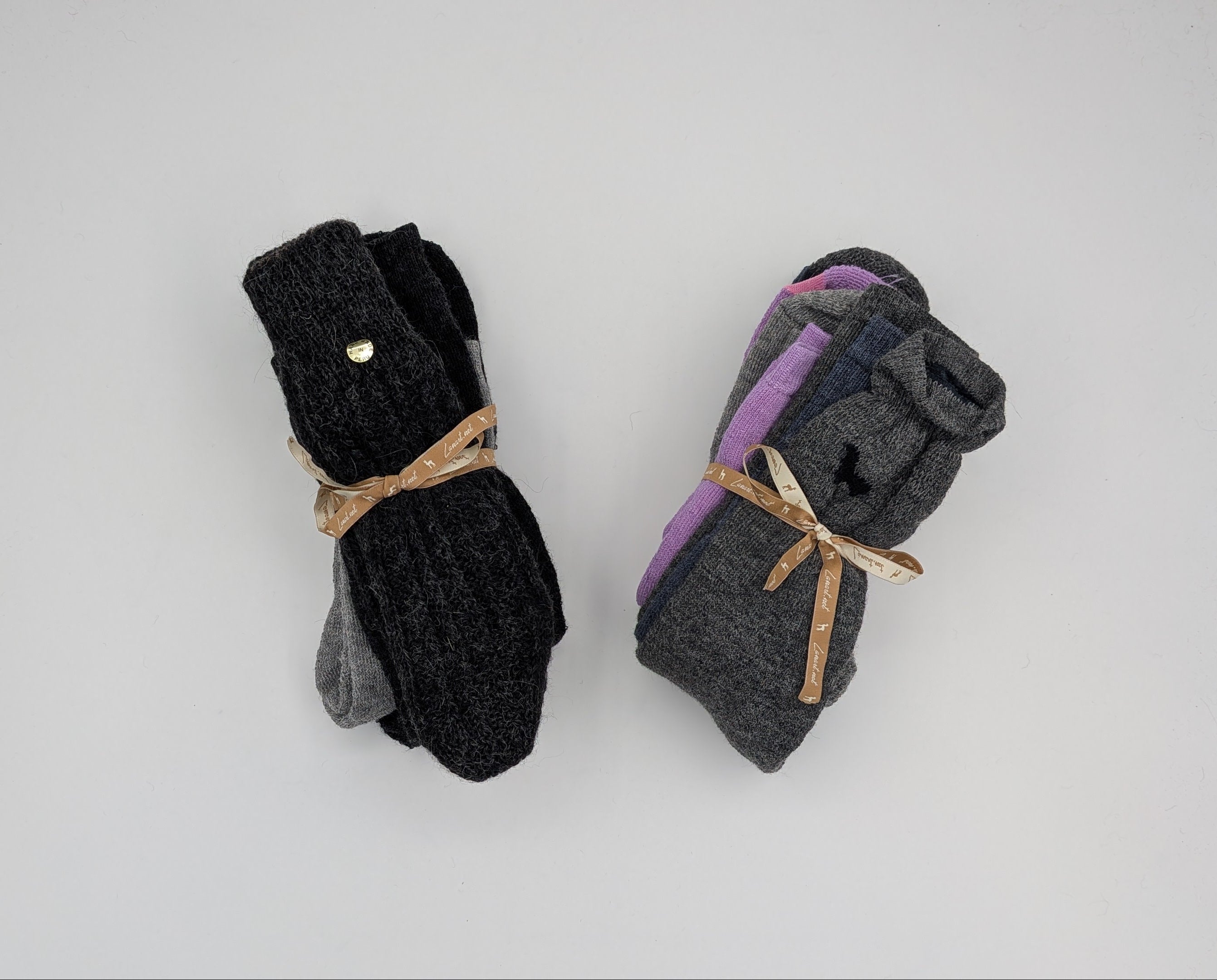 Two pairs of folded socks on a white background. The left pair is black with a small gold button and tied with a tan ribbon.