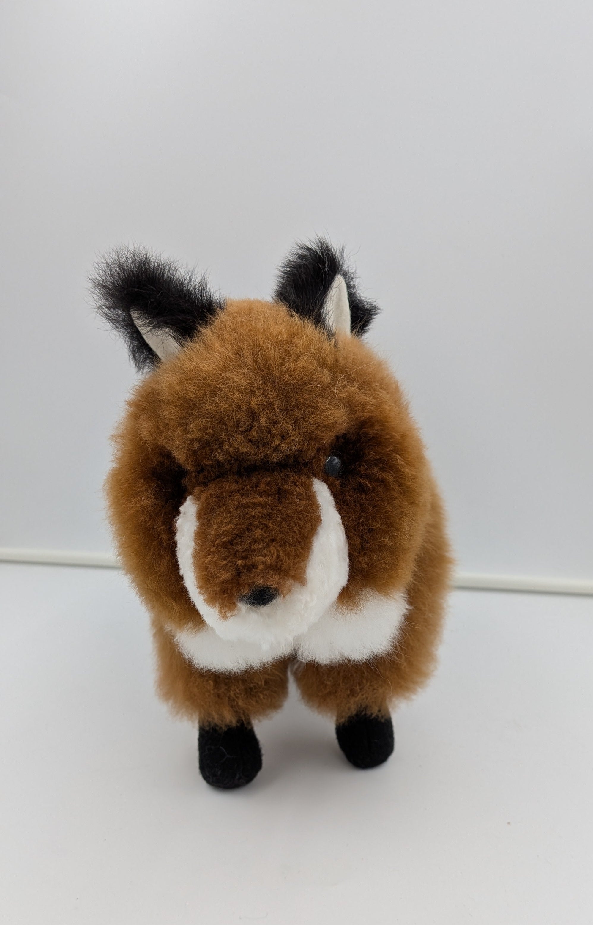 A plush toy fox with brown fur, a white muzzle and chest, and black ears, eyes, and paws, standing against a plain white background.
