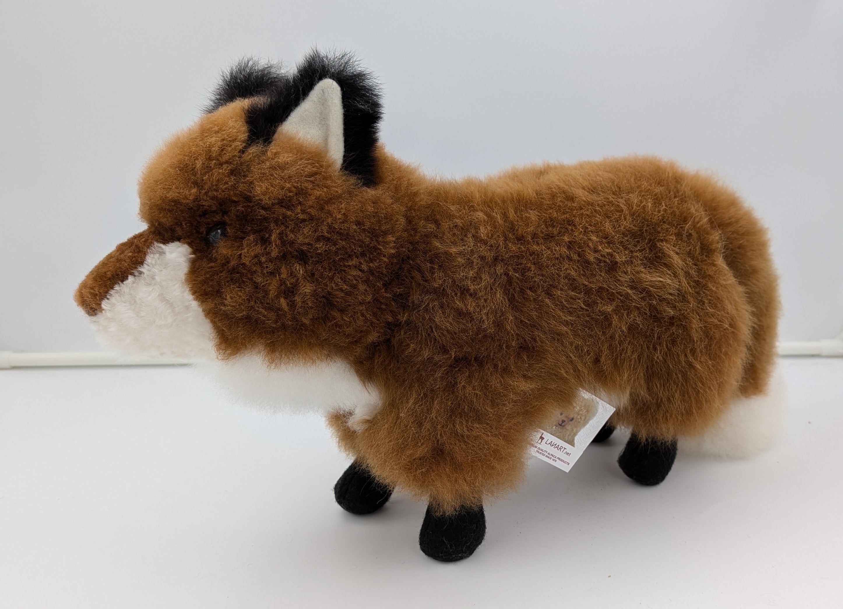 A plush toy fox with brown fur, a white muzzle and underbelly, black ears, and black legs, standing on a white studio background.