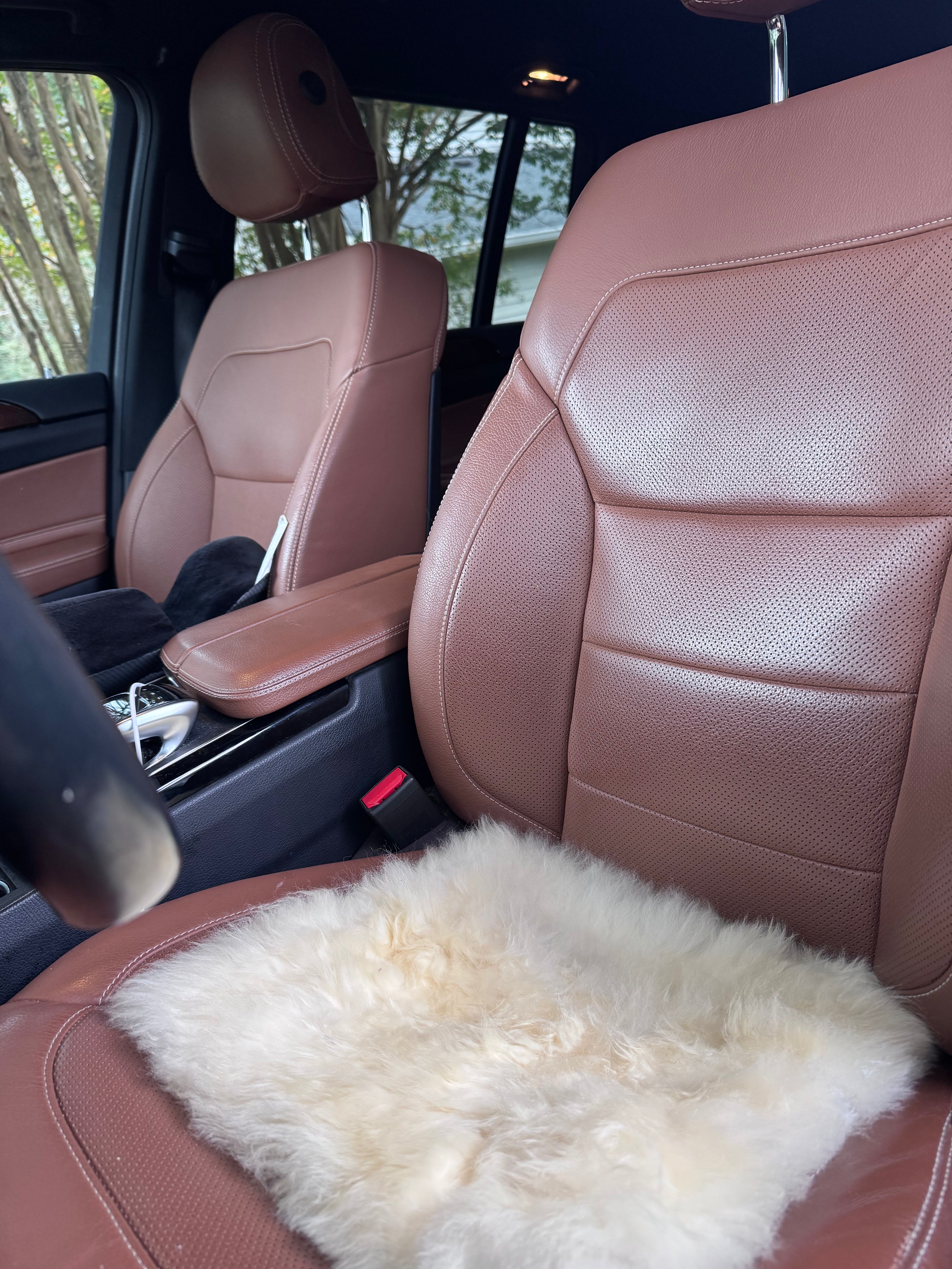 A fluffy cream-colored salpaca-shearling seat pad displayed on the front passenger seat of a vehicle with tan leather seats.