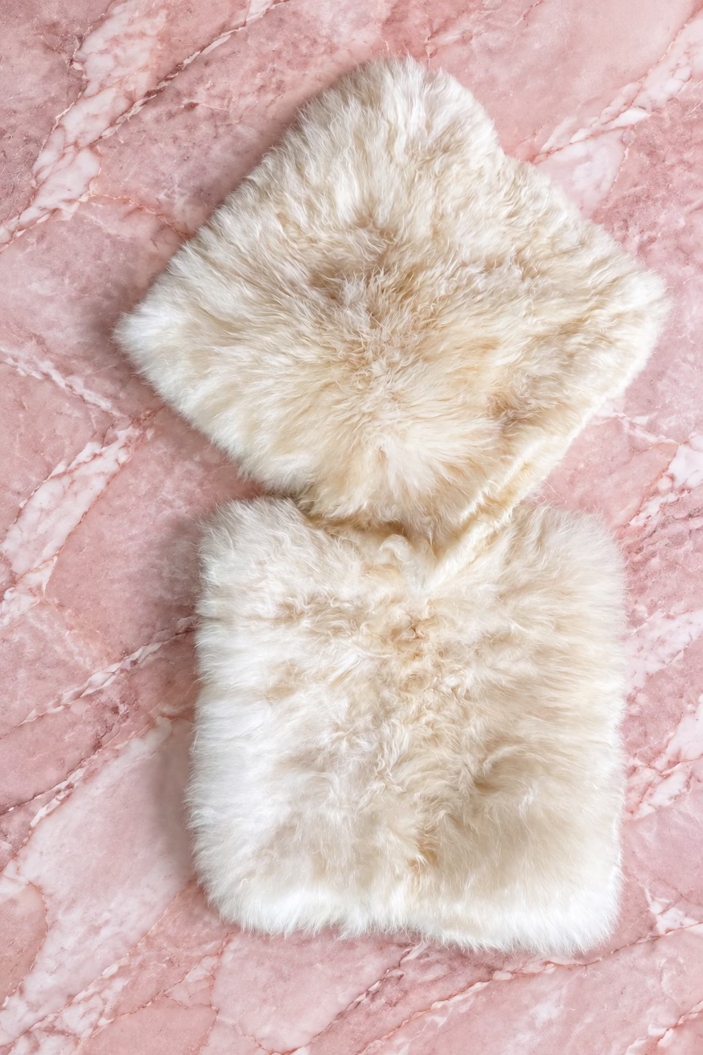 Two fluffy alpaca seat pads in natural cream and off-white tones, laid flat on a marble background.