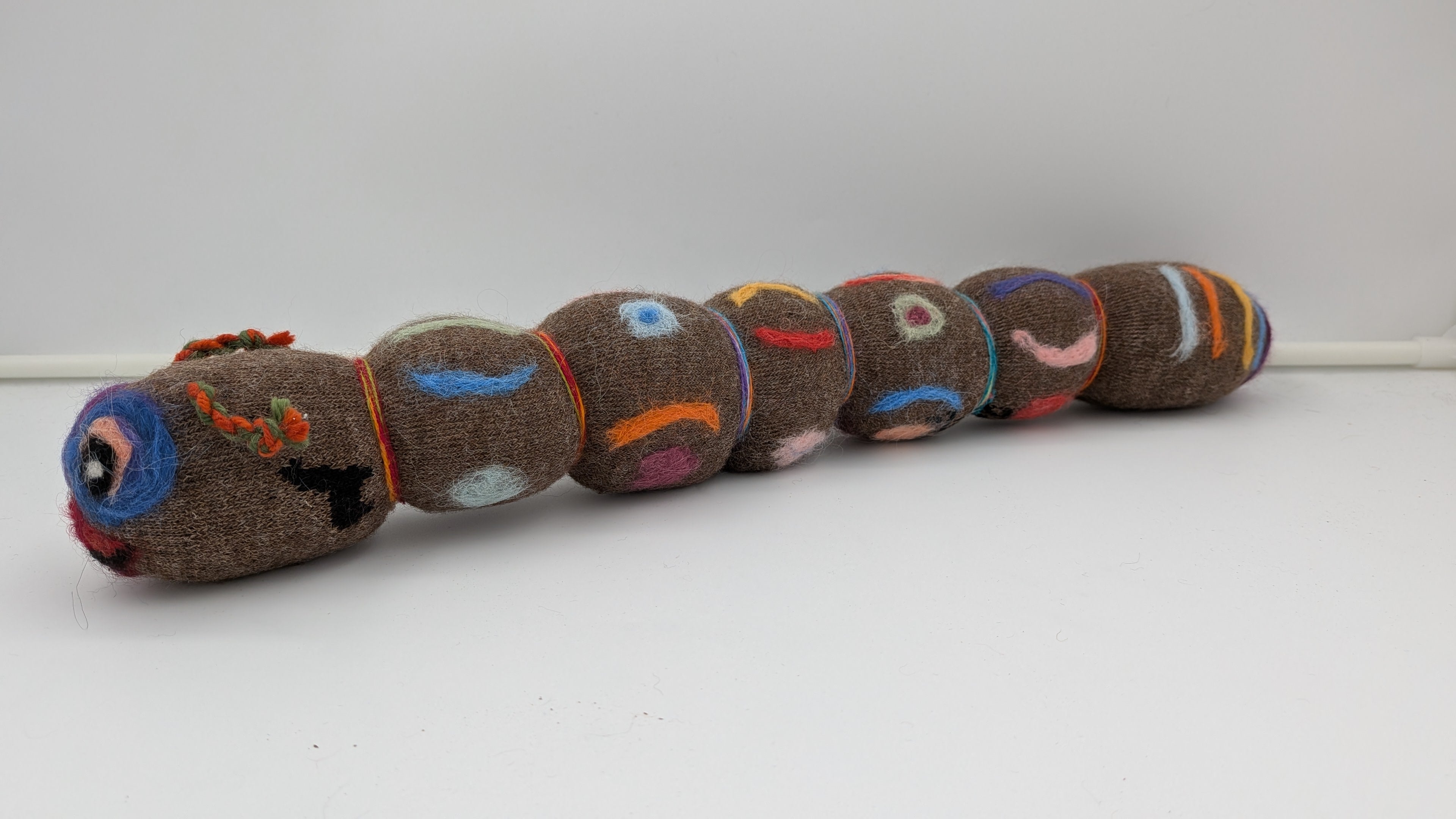 Toy caterpillar with colorful face designs on a white background
