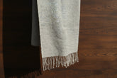 Gray and pearl textured light weight scarf with fringes on a wooden surface