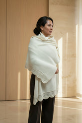 A woman wearing a cream-colored knit shawl with a scalloped edge.
