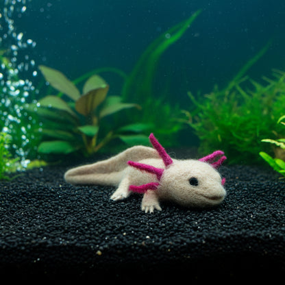 A felted alpaca sculpture resembling an Axolotl with beige body and pink protrusions on its back.