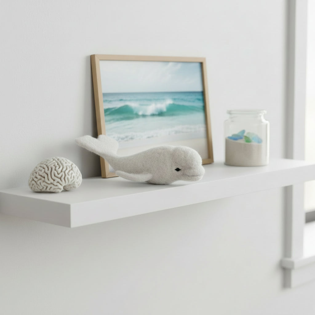 Lanart White alpaca fiber beluga whale toy on a shelf with a framed picture of waves and a small jar.