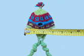 A handmade multicolor knit hat with a pom-pom next to a yellow measuring tape on a light surface.