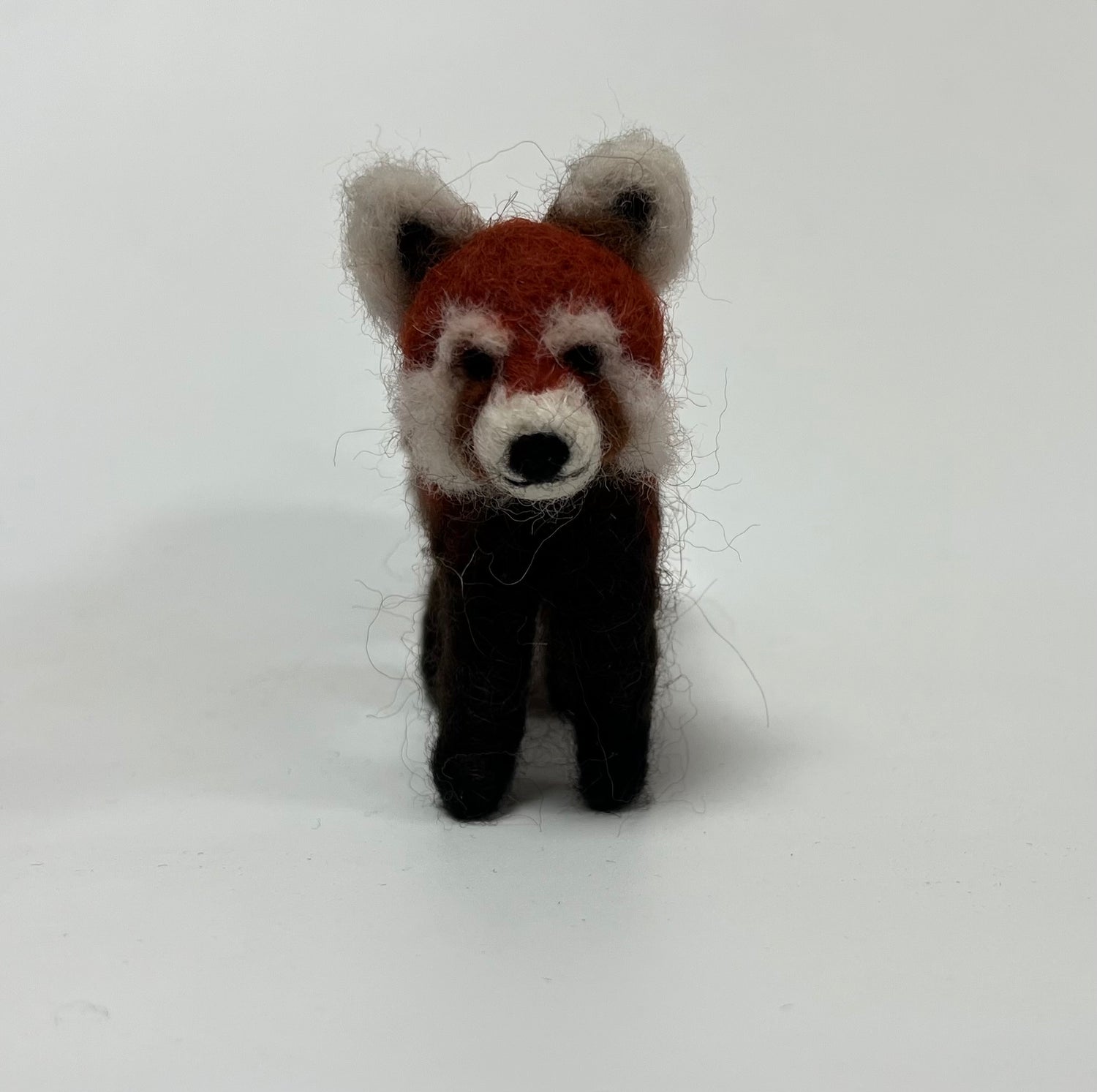 A handcrafted felted wool toy red panda standing upright against a plain white background.