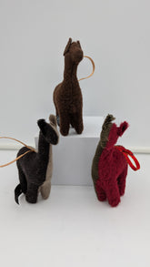 Three small felt llama or alpaca-shaped ornaments in brown, black, and red, each with a looped string and hanging loop, displayed on a white block against a light gray background.
