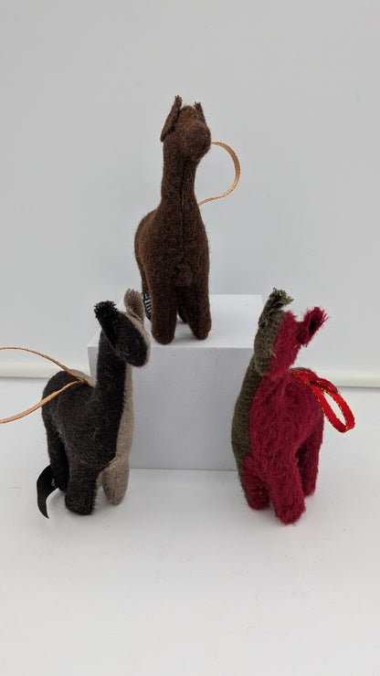 Three small felt llama or alpaca-shaped ornaments in brown, black, and red, each with a looped string and hanging loop, displayed on a white block against a light gray background.