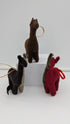 Three small felt llama or alpaca-shaped ornaments in brown, black, and red, each with a looped string and hanging loop, displayed on a white block against a light gray background.