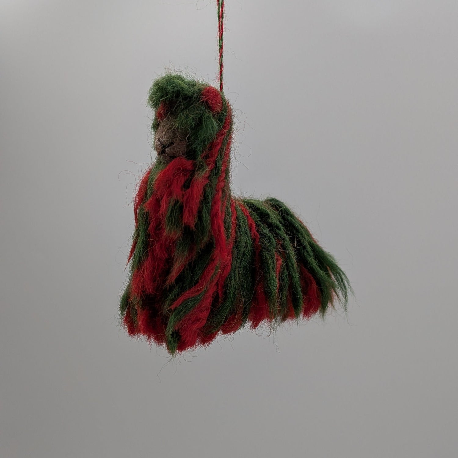 Decorative item resembling a horse made of red and green fabric hanging from a string against a white background.