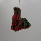 Decorative item resembling a horse made of red and green fabric hanging from a string against a white background.