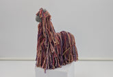 yarn alpaca llama sculpture on a white pedestal against a light gray background