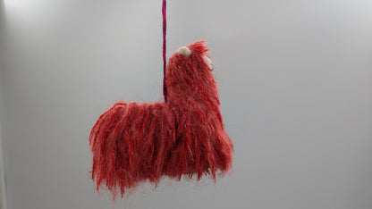 Red fluffy toy llama hanging against a plain background