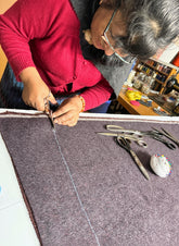 Person cutting a piece of baby alpaca fabric with scissors in a workshop setting.
