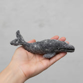 Hand holding a felt whale toy against a gray background