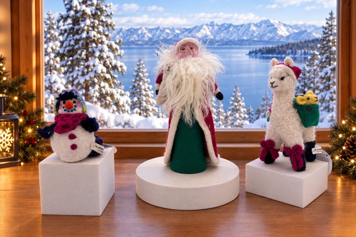 Three handmade wool felt holiday ornaments displayed on white pedestals: a snowman with a pink scarf, a Santa Claus figure with a white beard, and a white alpaca carrying a green sack.