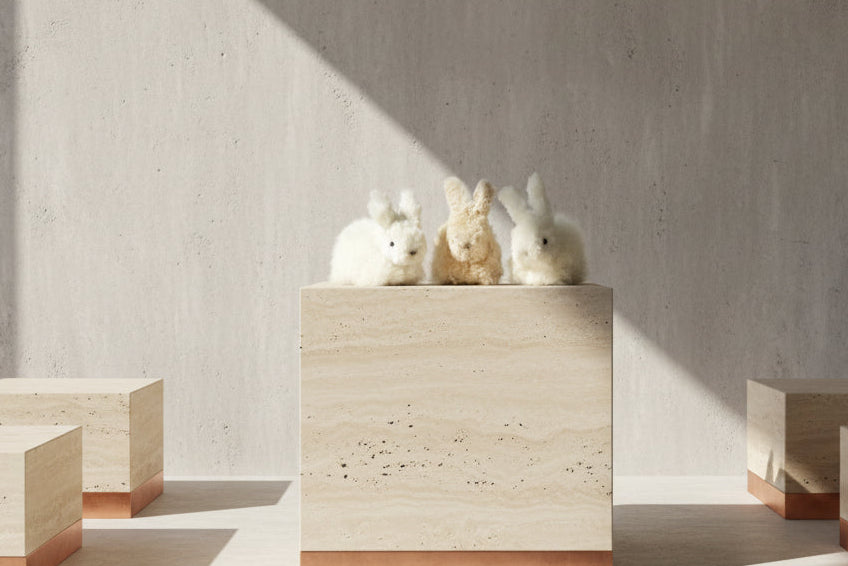 Three fluffy fleece rabbit toys in white, cream, and white are sitting on a gallery display