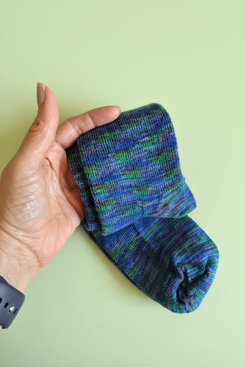 A pair of folded variegated knit socks held in a person&