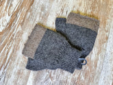 A pair of hand-knit fingerless gloves in a striped pattern of dark gray and light brown, displayed on a rustic, light-colored wooden surface.