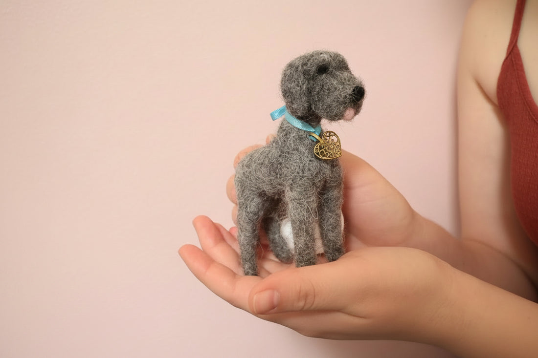 Small needle-felted dog held in hands with a textured gray background