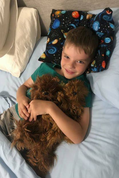 Child lying on a bed with a dog, surrounded by pillows including one with space design