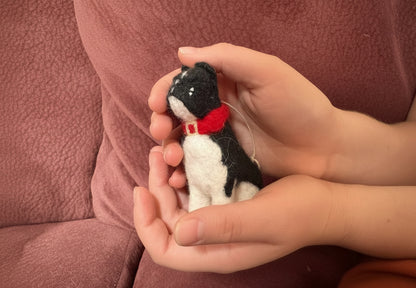 Hand holding a small felted french bulldog cradled in hands with a red collar