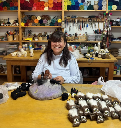 Jenny sitting at a table with various small needle felting animals and her tools on the wall.