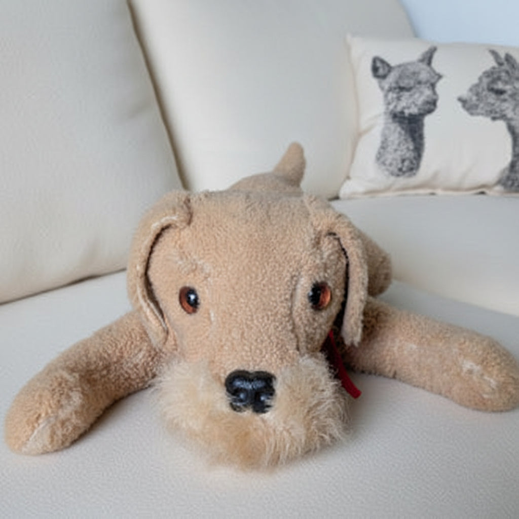 Stuffed dog toy on a striped couch with a pillow featuring animal designs.