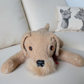 Stuffed dog toy on a striped couch with a pillow featuring animal designs.