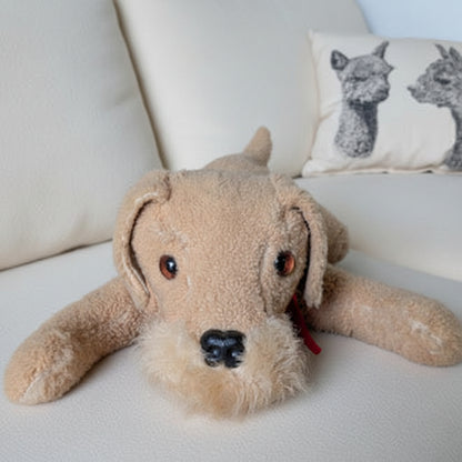 Stuffed dog toy on a striped couch with a pillow featuring animal designs.
