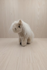 A small plush toy horse or pony with fluffy cream and white fur, standing on a plain white surface against a white background.