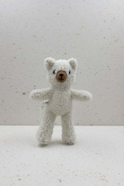 A small white teddy bear plush toy with a brown button nose and black embroidered eyes, mounted on a clear stand against a plain light gray wall.