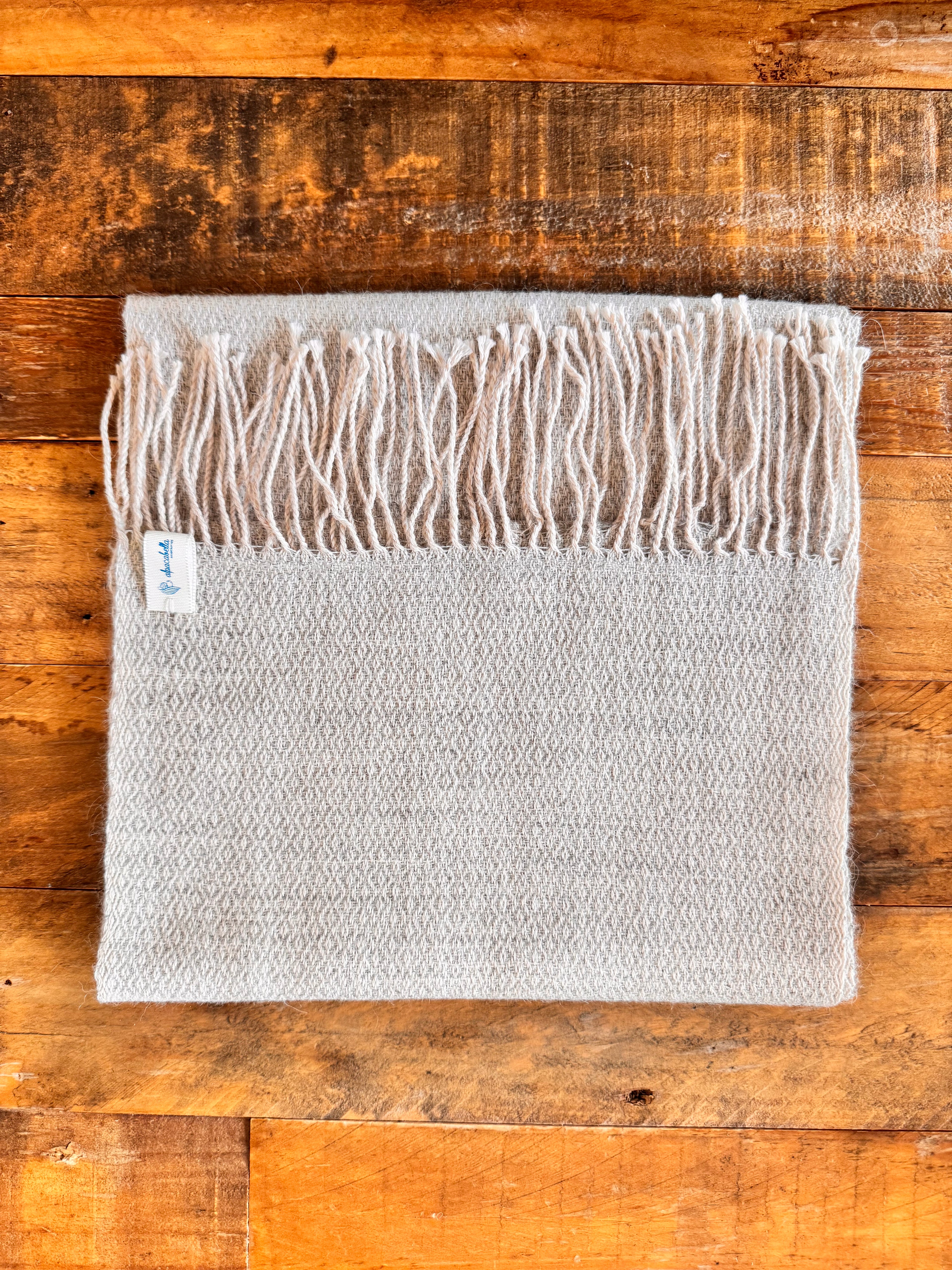 Gray textured lightweight
 with fringe on a wooden surface