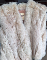 A large, fluffy fur vest in  beige color, displayed on a black hanger.