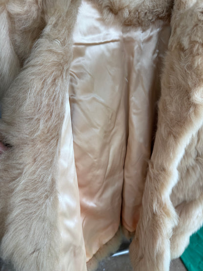 Close-up of a beige fur vest with a shiny cream satin lining, showing the texture of the fur and the interior.