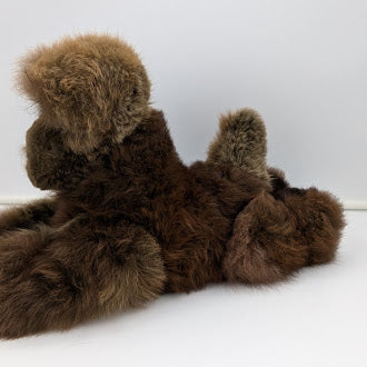 Brown alpaca fur dog stuffed animal lying on a white surface with a white background