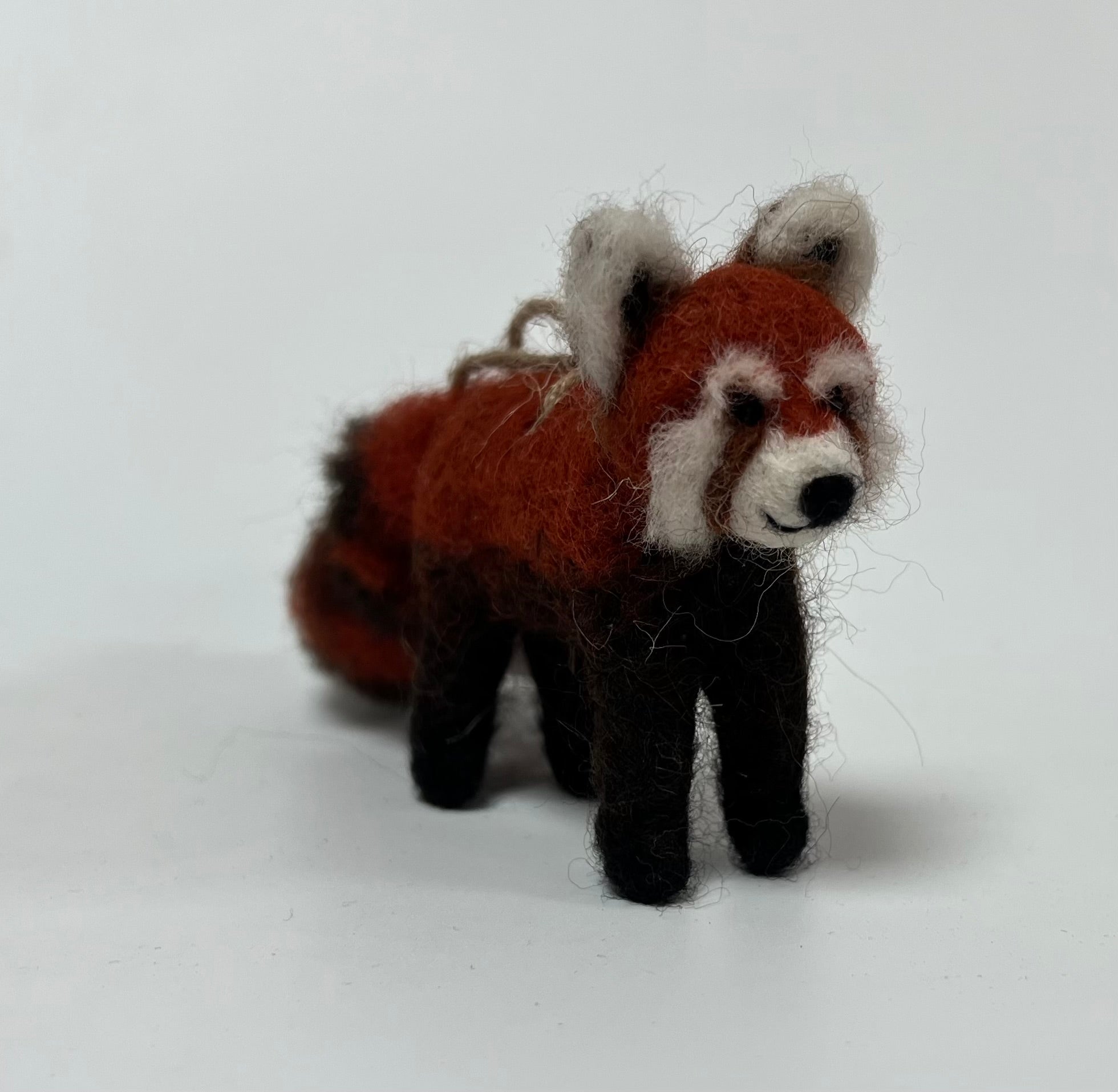 A small felted wool red panda figurine standing on a plain white studio background.