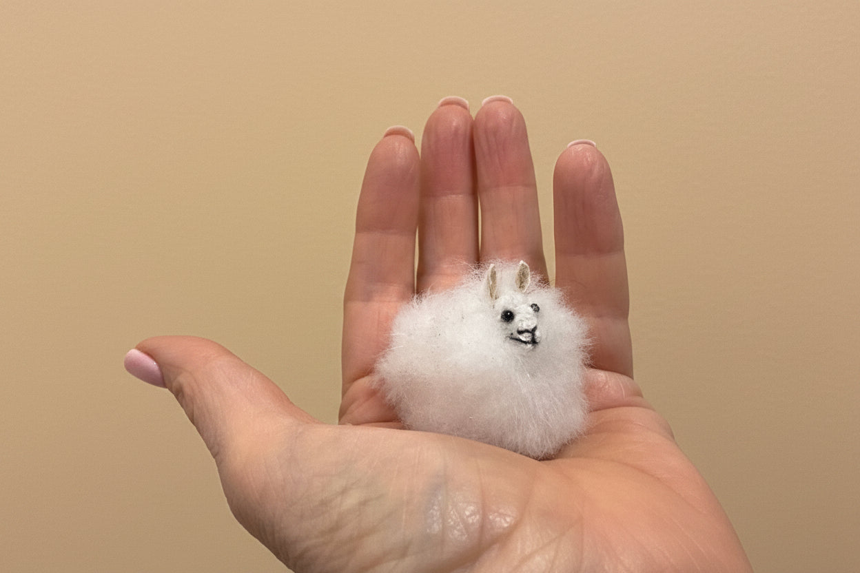 Small white plush toy held in a hand against a plain background