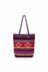 A colorful woven tote bag with braided handles, featuring a Southwestern geometric pattern in red, pink, purple, green, and beige, resting on a white shelf.